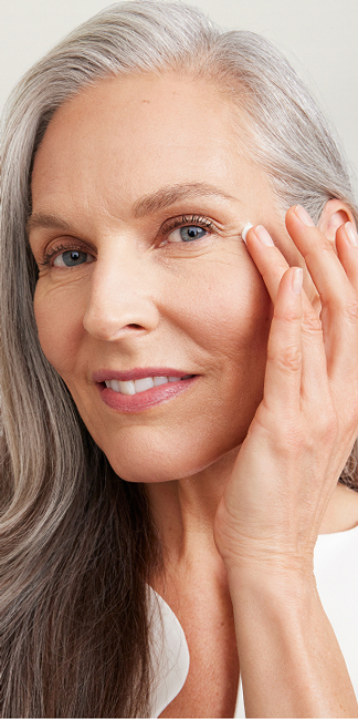 Mujer con piel madura y luminosa aplicando crema para el contorno de ojos.